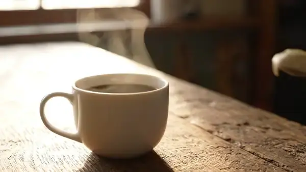 A spoon slowly stirring pale paste into a white mug of black coffee, the paste dissolving into swirls