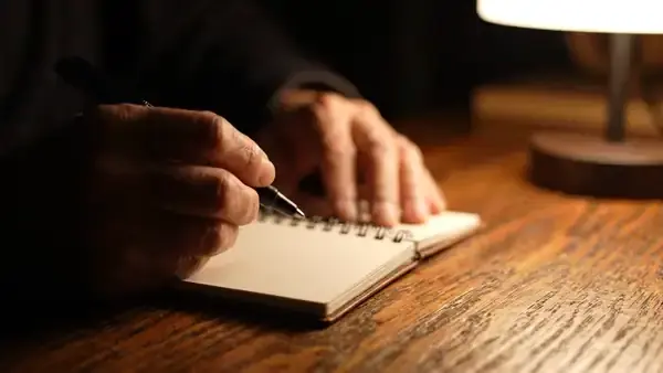 Hands writing one short line in a small pocket notebook in the evening and closing the cover